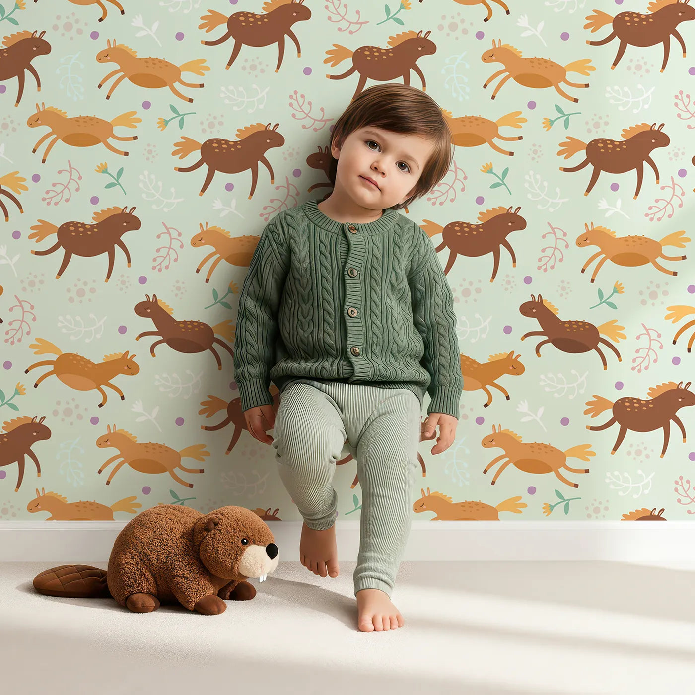Lovely child standing in front of Whimsy Tots Dreamy Pony Meadow Wallpaper in Soft Mint Green with horse, flower, leaf, dot in design.
