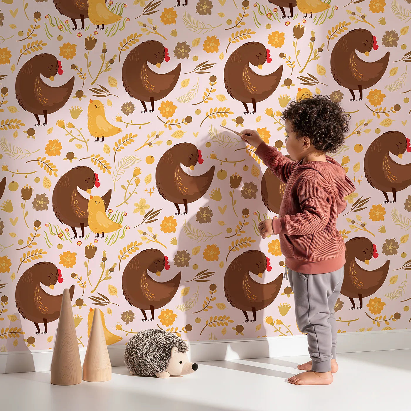 Lovely child standing in front of Whimsy Tots Hen and Chick Meadow Wallpaper in Blush Nest Pink with chicken, chick, flower, leaf in design.