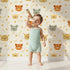 Lovely child standing in front of Whimsy Tots Outback Snuggle Faces Wallpaper in Cream with koala, fox, lynx, feather, berry in design. Lovely child standing in front of Whimsy Tots Outback Snuggle Faces Wallpaper in Cream with koala, fox, lynx, feather, berry in design.