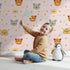 Lovely child standing in front of Whimsy Tots Outback Snuggle Faces Wallpaper in Blush Pink with koala, fox, lynx, feather, berry in design. Lovely child standing in front of Whimsy Tots Outback Snuggle Faces Wallpaper in Blush Pink with koala, fox, lynx, feather, berry in design.