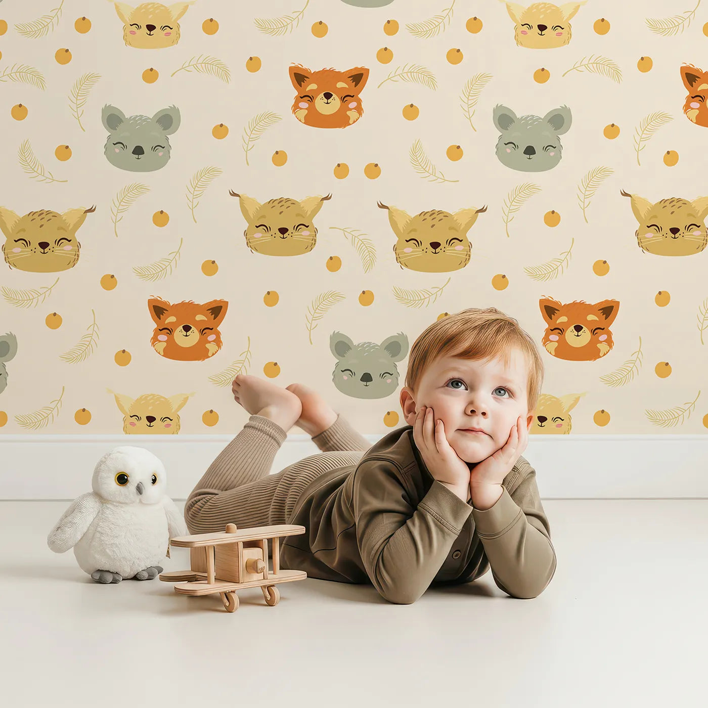 Lovely child standing in front of Whimsy Tots Outback Snuggle Faces Wallpaper in Sandstone with koala, fox, lynx, feather, berry in design.