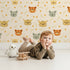 Lovely child standing in front of Whimsy Tots Outback Snuggle Faces Wallpaper in Sandstone with koala, fox, lynx, feather, berry in design. Lovely child standing in front of Whimsy Tots Outback Snuggle Faces Wallpaper in Sandstone with koala, fox, lynx, feather, berry in design.