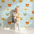 Lovely child standing in front of Whimsy Tots Outback Snuggle Faces Wallpaper in Sky Blue with koala, fox, lynx, feather, berry in design. Lovely child standing in front of Whimsy Tots Outback Snuggle Faces Wallpaper in Sky Blue with koala, fox, lynx, feather, berry in design.