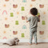 Lovely child standing in front of Whimsy Tots Garden Hop and Snail Trail Wallpaper in Cream with frog, snail, dragonfly, rainbow, sun, flower in design. Lovely child standing in front of Whimsy Tots Garden Hop and Snail Trail Wallpaper in Cream with frog, snail, dragonfly, rainbow, sun, flower in design.