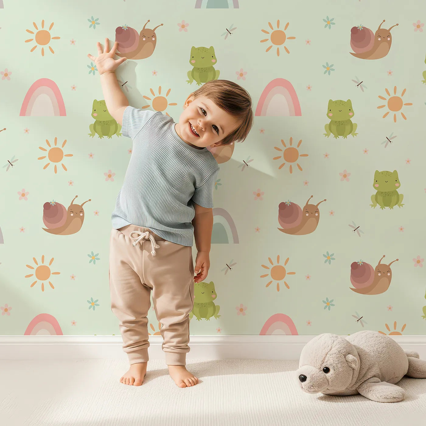Lovely child standing in front of Whimsy Tots Garden Hop and Snail Trail Wallpaper in Mint Green with frog, snail, dragonfly, rainbow, sun, flower in design.