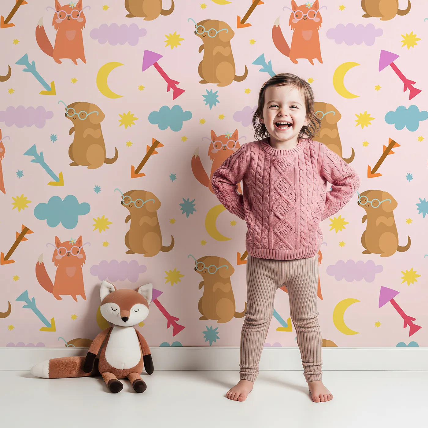Lovely child standing in front of Whimsy Tots Arrow Pup and Foxy Night Parade Wallpaper in Blush Pink with dog, fox, moon, arrow, star, cloud in design.