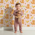 Lovely child standing in front of Whimsy Tots Fox and Finch Woodland Waltz Wallpaper in Blush Pink with fox, bird, acorn, leaf, flower in design. Lovely child standing in front of Whimsy Tots Fox and Finch Woodland Waltz Wallpaper in Blush Pink with fox, bird, acorn, leaf, flower in design.