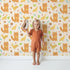 Lovely child standing in front of Whimsy Tots Fox and Finch Woodland Waltz Wallpaper in Sandstone with fox, bird, acorn, leaf, flower in design. Lovely child standing in front of Whimsy Tots Fox and Finch Woodland Waltz Wallpaper in Sandstone with fox, bird, acorn, leaf, flower in design.