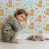 Lovely child standing in front of Whimsy Tots Fox and Finch Woodland Waltz Wallpaper in Sky Blue with fox, bird, acorn, leaf, flower in design. Lovely child standing in front of Whimsy Tots Fox and Finch Woodland Waltz Wallpaper in Sky Blue with fox, bird, acorn, leaf, flower in design.