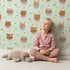 Lovely child standing in front of Whimsy Tots Heart Bloom Critters Wallpaper in Mint Green with bear, rabbit, owl, heart, flower, cloud in design. Lovely child standing in front of Whimsy Tots Heart Bloom Critters Wallpaper in Mint Green with bear, rabbit, owl, heart, flower, cloud in design.