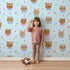 Lovely child standing in front of Whimsy Tots Heart Bloom Critters Wallpaper in Blue with bear, rabbit, owl, heart, flower, cloud in design. Lovely child standing in front of Whimsy Tots Heart Bloom Critters Wallpaper in Blue with bear, rabbit, owl, heart, flower, cloud in design.