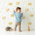 Lovely child standing in front of Whimsy Tots Snail Meadow Cuddle Parade Wallpaper in White with snail, flower, leaf in design. Lovely child standing in front of Whimsy Tots Snail Meadow Cuddle Parade Wallpaper in White with snail, flower, leaf in design.