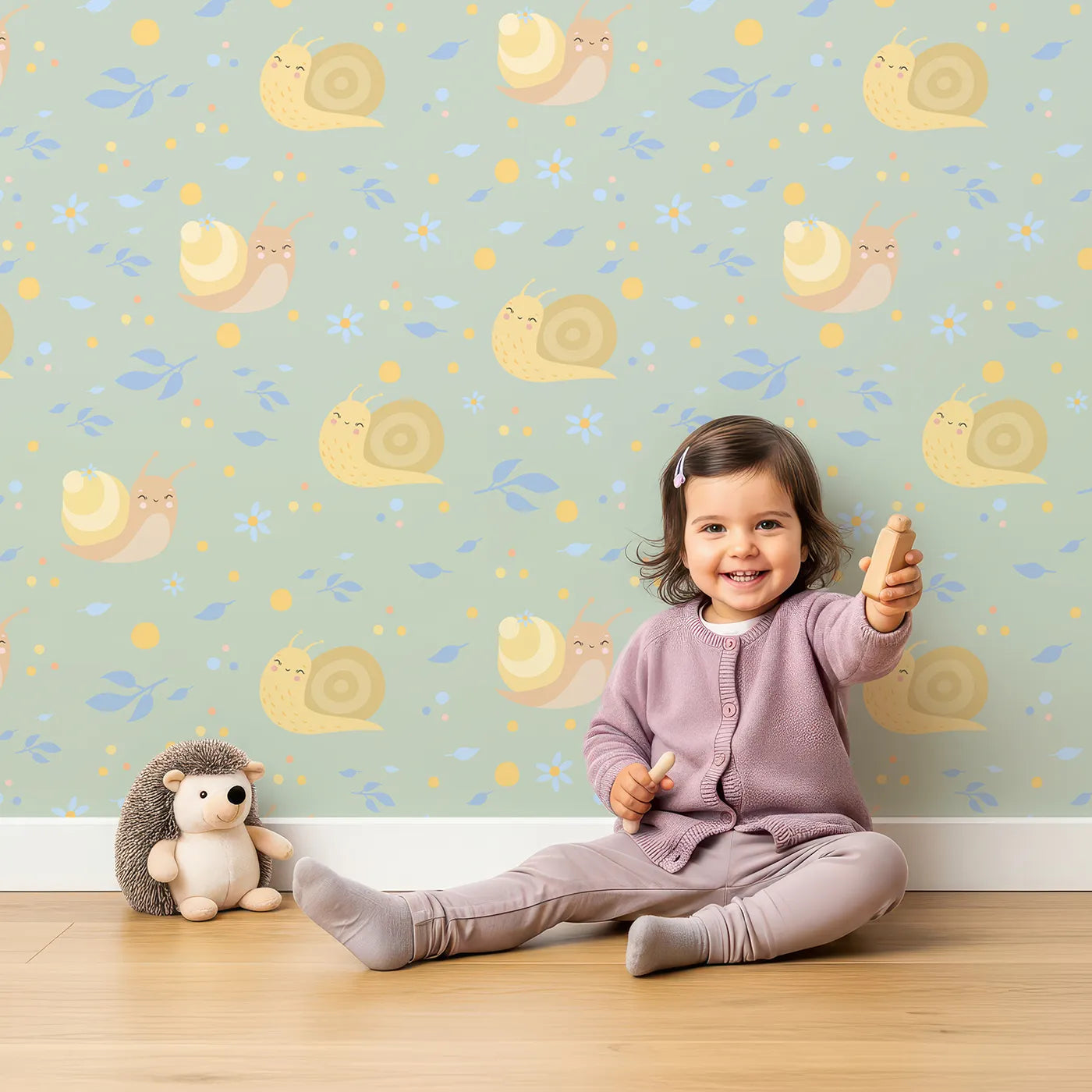 Lovely child standing in front of Whimsy Tots Snail Meadow Cuddle Parade Wallpaper in Sage Green with snail, flower, leaf in design.