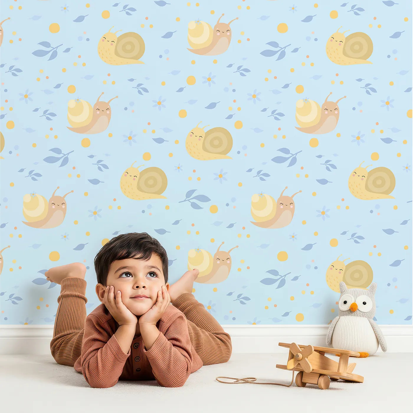 Lovely child standing in front of Whimsy Tots Snail Meadow Cuddle Parade Wallpaper in Sky Blue with snail, flower, leaf in design.
