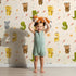 Lovely child standing in front of Whimsy Tots Wild Heart Animal Parade Wallpaper in Cream with giraffe, koala, leopard, monkey, tiger, crocodile, heart, arrow, star in design. Lovely child standing in front of Whimsy Tots Wild Heart Animal Parade Wallpaper in Cream with giraffe, koala, leopard, monkey, tiger, crocodile, heart, arrow, star in design.