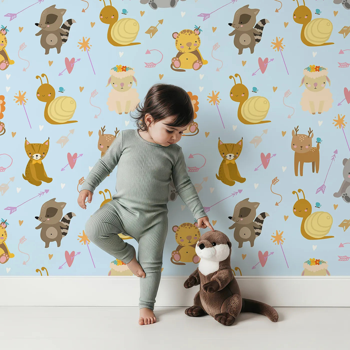Lovely child standing in front of Whimsy Tots Magic Meadow Friends Wallpaper in Blue with deer, koala, leopard, lion, raccoon, snail, arrow, wand, heart in design.