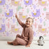 Lovely child standing in front of Whimsy Tots Bouncing Llama Fiesta Wallpaper in Pink Blush with llama, cactus, flower, confetti in design. Lovely child standing in front of Whimsy Tots Bouncing Llama Fiesta Wallpaper in Pink Blush with llama, cactus, flower, confetti in design.