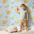 Lovely child standing in front of Whimsy Tots Tweeting Lovebirds Wallpaper in Blue with bird, owl, flower, heart, branch in design. Lovely child standing in front of Whimsy Tots Tweeting Lovebirds Wallpaper in Blue with bird, owl, flower, heart, branch in design.