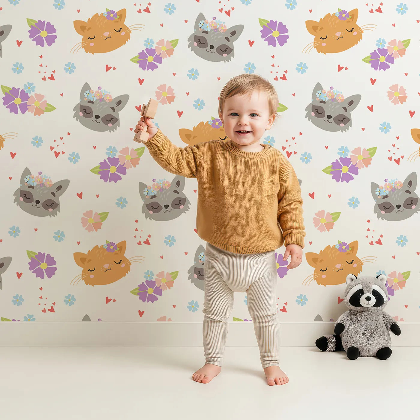 Lovely child standing in front of Whimsy Tots Meadow Snuggle Faces Wallpaper in White with cat, raccoon, flower, heart in design.