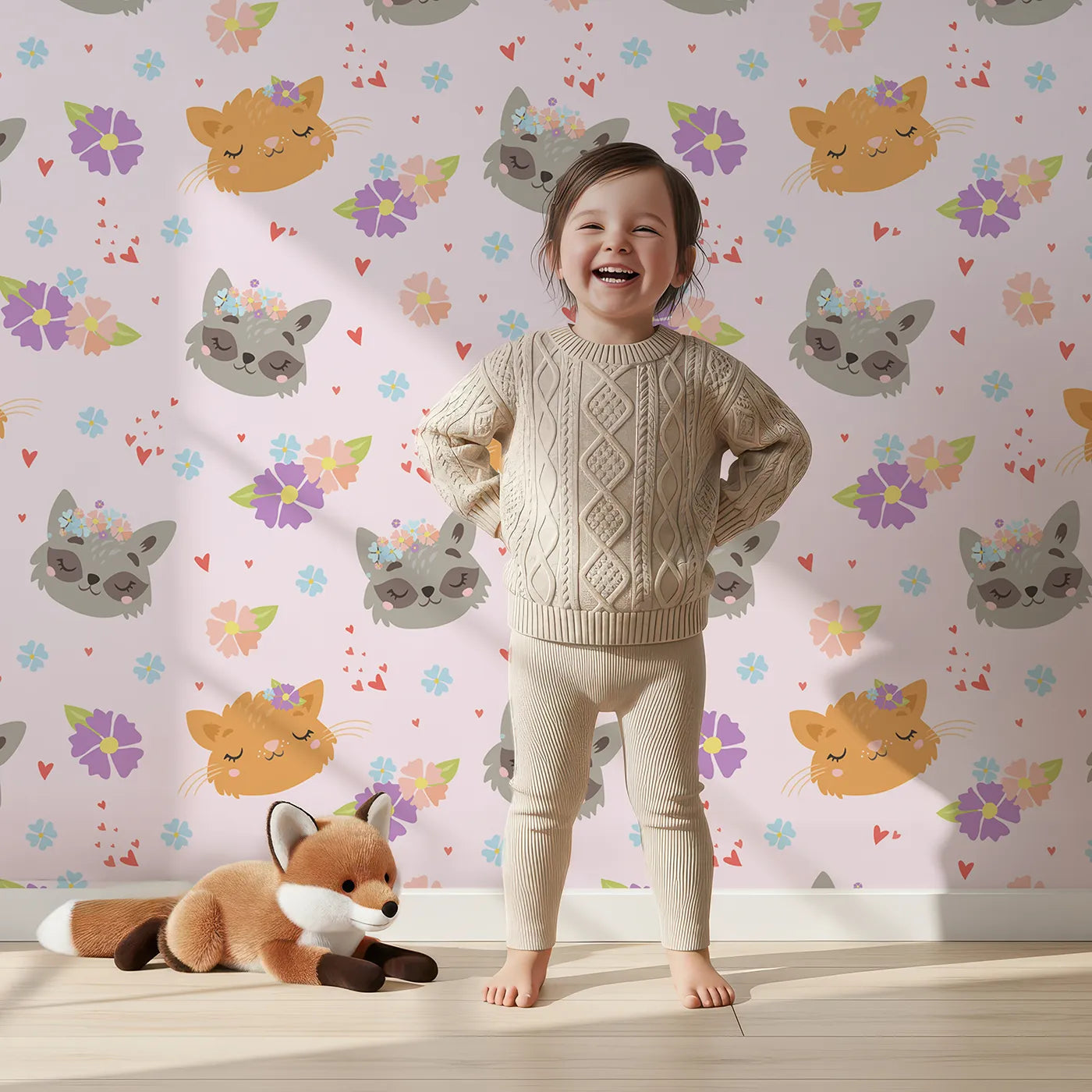 Lovely child standing in front of Whimsy Tots Meadow Snuggle Faces Wallpaper in Pink with cat, raccoon, flower, heart in design.
