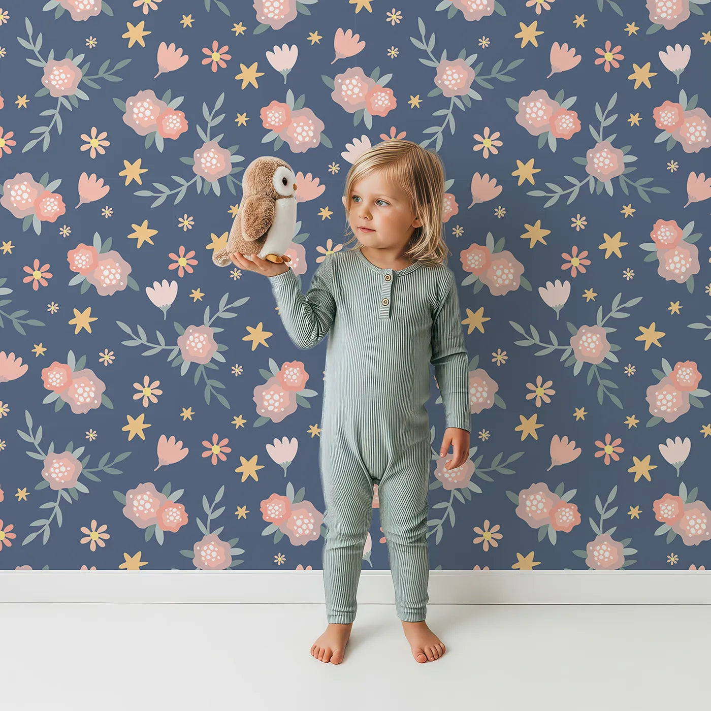 Lovely child standing in front of Whimsy Tots Twilight Wildflower Waltz Wallpaper in Blue with flower, star, leaf in design.