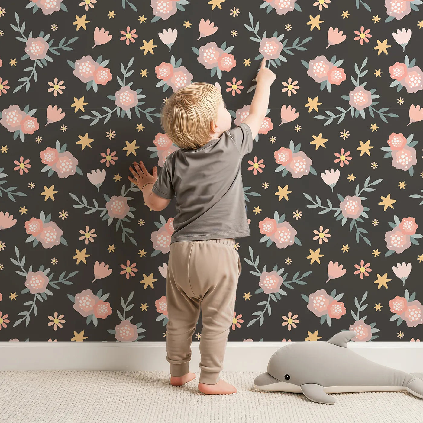 Lovely child standing in front of Whimsy Tots Twilight Wildflower Waltz Wallpaper in Charcoal Gray with flower, star, leaf in design.