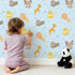 Lovely child standing in front of Whimsy Tots Safari Buddies Parade Wallpaper in Blue with lion, giraffe, elephant, hippo, tiger, arrow in design. Lovely child standing in front of Whimsy Tots Safari Buddies Parade Wallpaper in Blue with lion, giraffe, elephant, hippo, tiger, arrow in design.