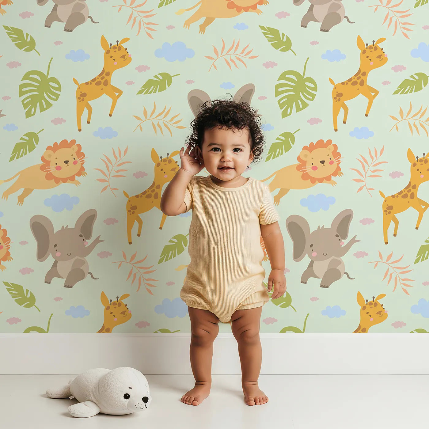 Lovely child standing in front of Whimsy Tots Jungle Leaf Pals Wallpaper in Mint Green with lion, giraffe, elephant, leaf, cloud in design.