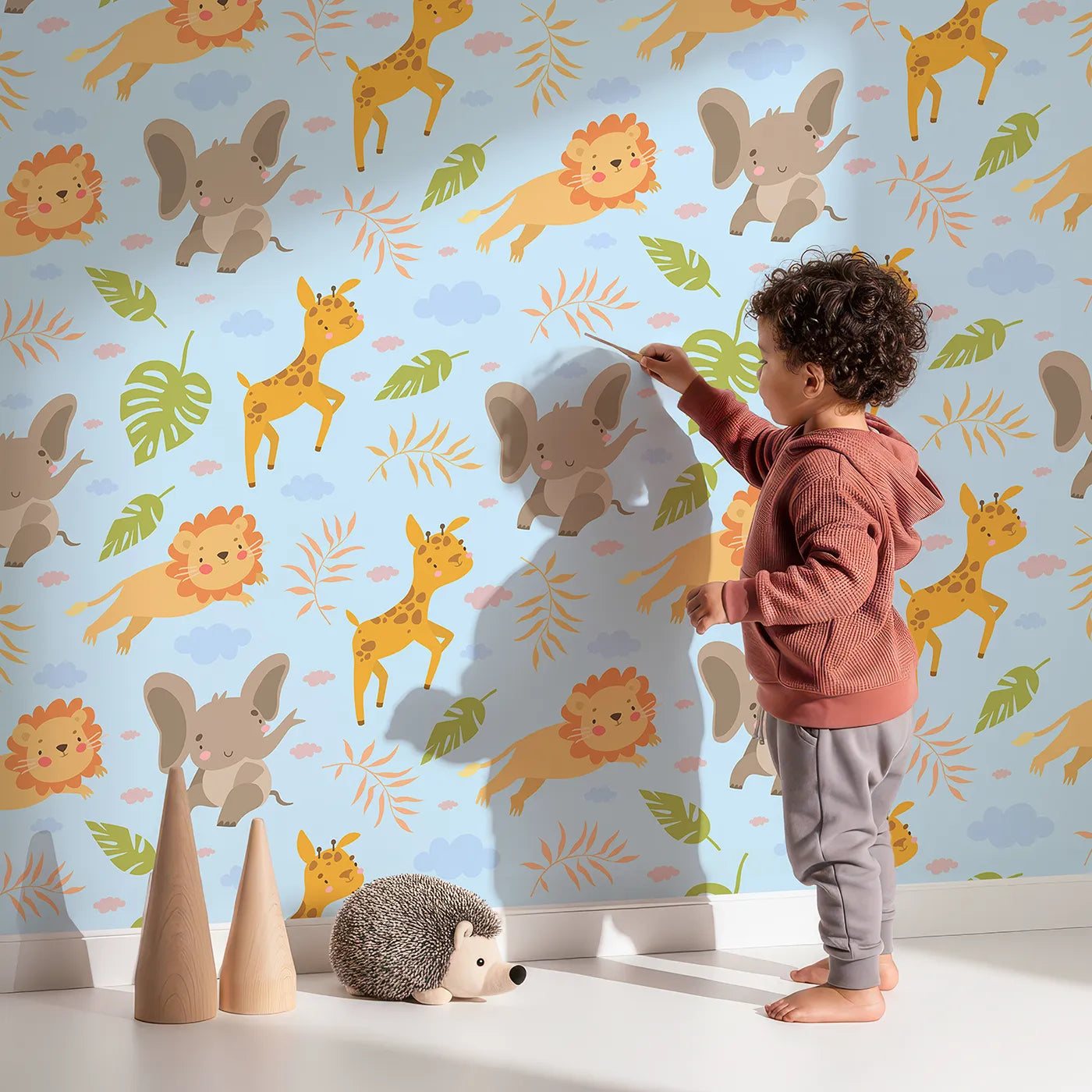 Lovely child standing in front of Whimsy Tots Jungle Leaf Pals Wallpaper in Blue with lion, giraffe, elephant, leaf, cloud in design.