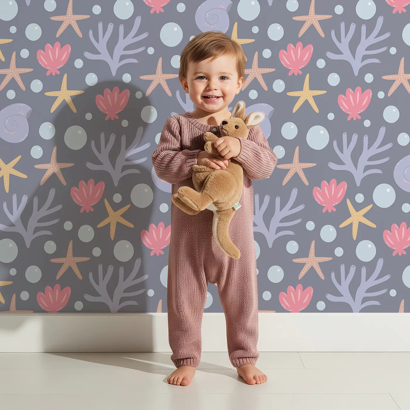 Lovely child standing in front of Whimsy Tots Starry Coral Garden Wallpaper in Deep Sea Gray with starfish, coral, shell, bubble in design.