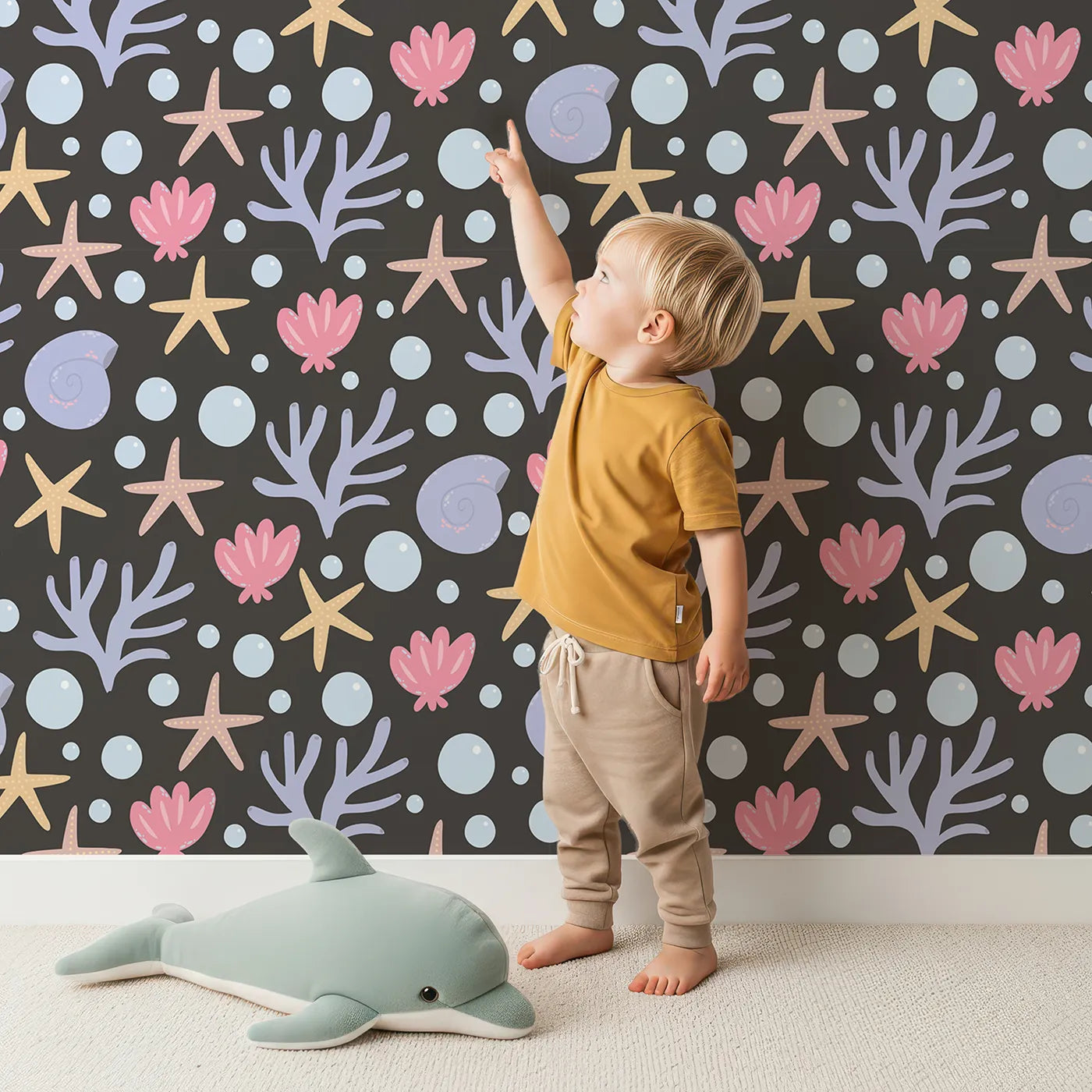 Lovely child standing in front of Whimsy Tots Starry Coral Garden Wallpaper in Charcoal Gray with starfish, coral, shell, bubble in design.
