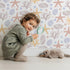 Lovely child standing in front of Whimsy Tots Pebble Shoreline Calm Wallpaper in White with starfish, coral, shell, pebble, bubble in design. Lovely child standing in front of Whimsy Tots Pebble Shoreline Calm Wallpaper in White with starfish, coral, shell, pebble, bubble in design.