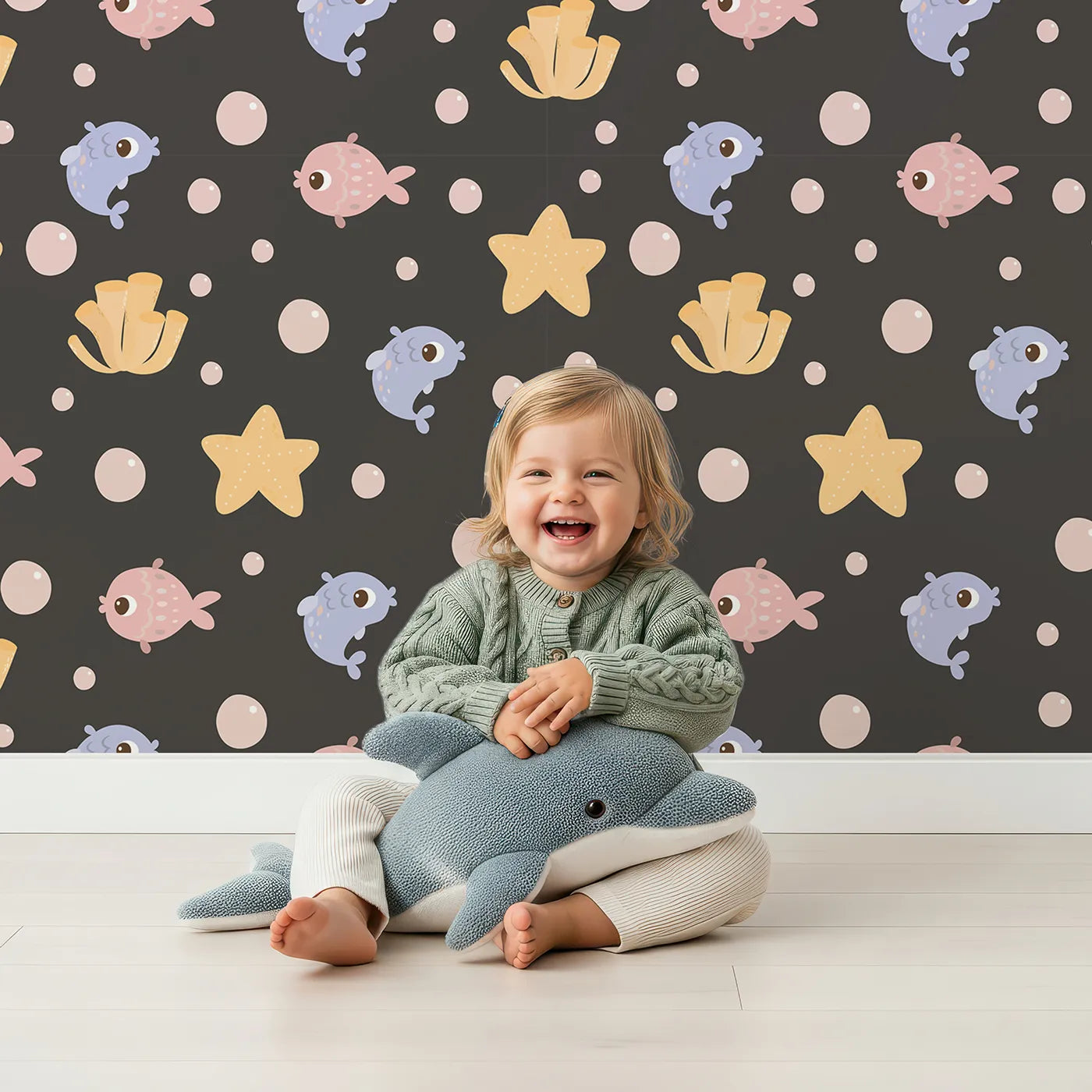 Lovely child standing in front of Whimsy Tots Bubblefish Coral Drift Wallpaper in Charcoal Gray with fish, coral, bubble, starfish in design.