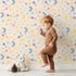 Lovely child standing in front of Whimsy Tots Starlit Wishes Wallpaper in Vanilla with moon, star, constellation, shooting star, galaxy in design. Lovely child standing in front of Whimsy Tots Starlit Wishes Wallpaper in Vanilla with moon, star, constellation, shooting star, galaxy in design.