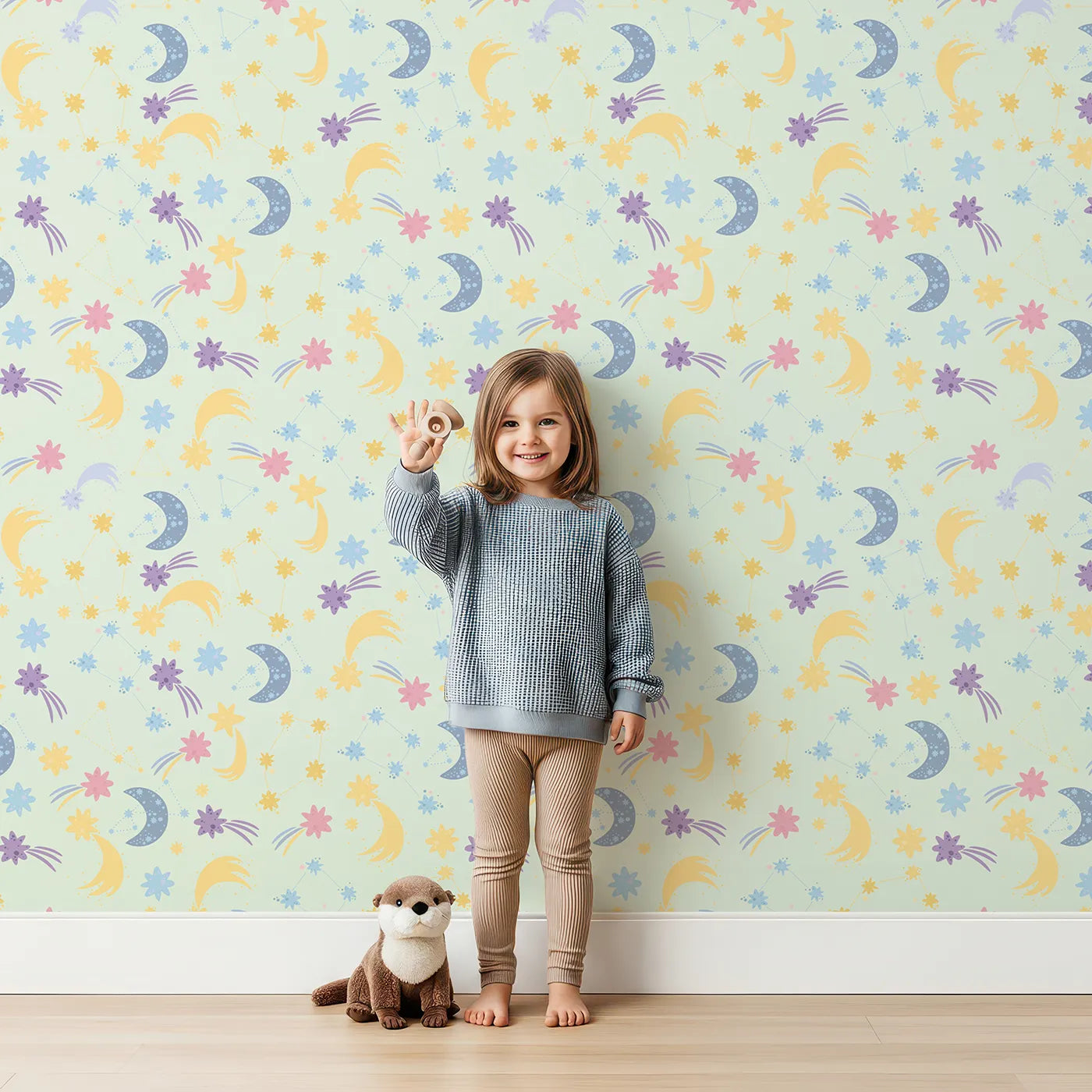 Lovely child standing in front of Whimsy Tots Starlit Wishes Wallpaper in Mint Green with moon, star, constellation, shooting star, galaxy in design.