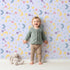 Lovely child standing in front of Whimsy Tots Starlit Wishes Wallpaper in Periwinkle with moon, star, constellation, shooting star, galaxy in design. Lovely child standing in front of Whimsy Tots Starlit Wishes Wallpaper in Periwinkle with moon, star, constellation, shooting star, galaxy in design.