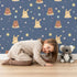 Lovely child standing in front of Whimsy Tots Starry Snuggle Pals Wallpaper in Navy Blue with bear, rabbit, star, heart, constellation in design. Lovely child standing in front of Whimsy Tots Starry Snuggle Pals Wallpaper in Navy Blue with bear, rabbit, star, heart, constellation in design.