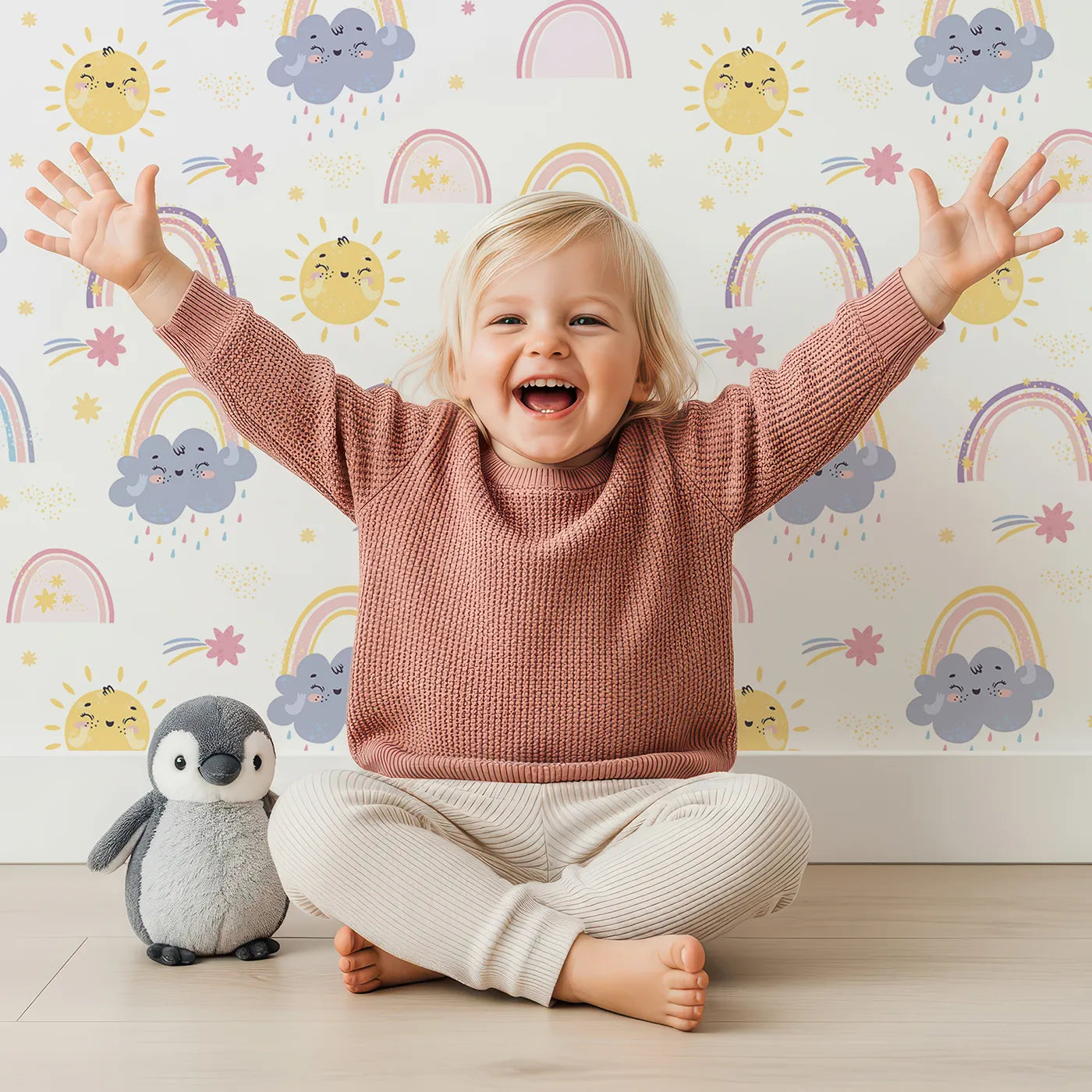 Lovely child standing in front of Whimsy Tots Sunshine After Rain Wallpaper with sun, cloud, rainbow, raindrop, star in design.