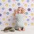 Lovely child standing in front of Whimsy Tots Planet Pals Orbit Parade Wallpaper in Lilac Lavender with planet, sun, moon, star, comet in design. Lovely child standing in front of Whimsy Tots Planet Pals Orbit Parade Wallpaper in Lilac Lavender with planet, sun, moon, star, comet in design.