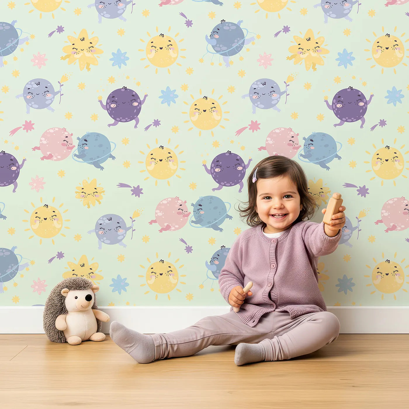 Lovely child standing in front of Whimsy Tots Planet Pals Orbit Parade Wallpaper in Mint Green with planet, sun, moon, star, comet in design.