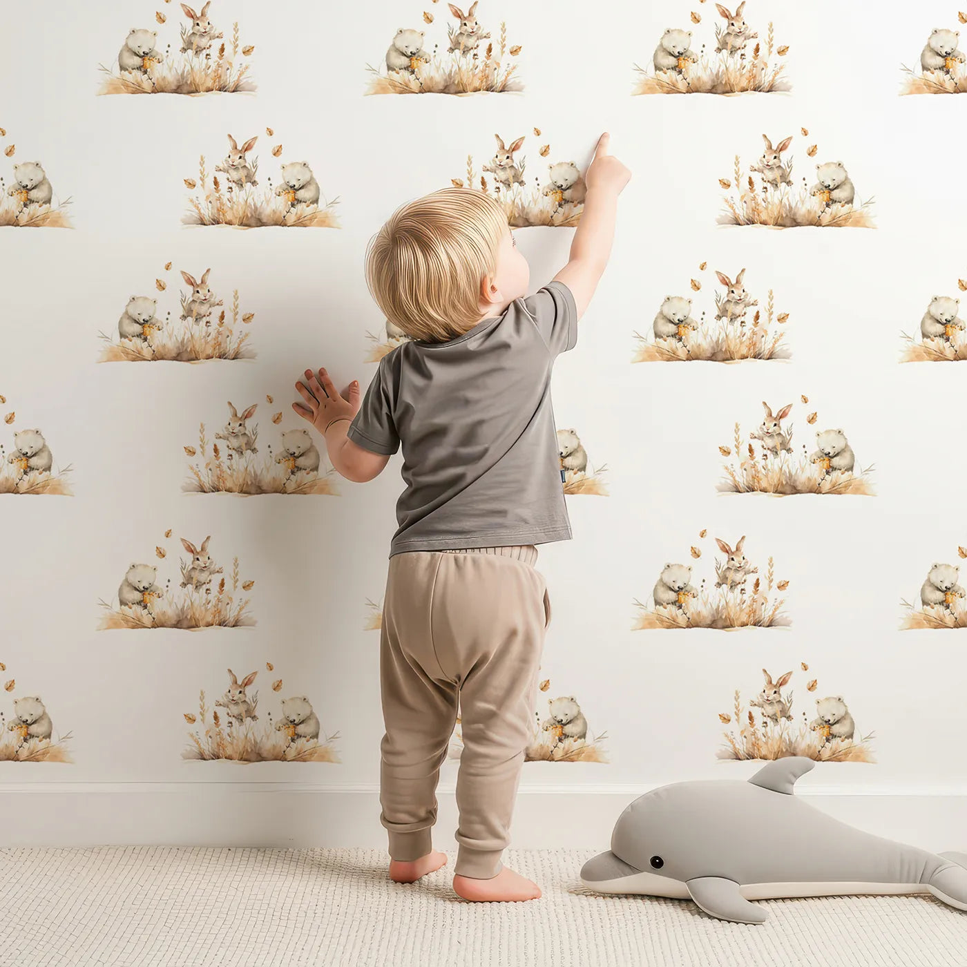 Lovely child standing in front of Whimsy Tots Wheatfield Snuggle Friends Wallpaper with bear, rabbit, wheat, leaf in design.