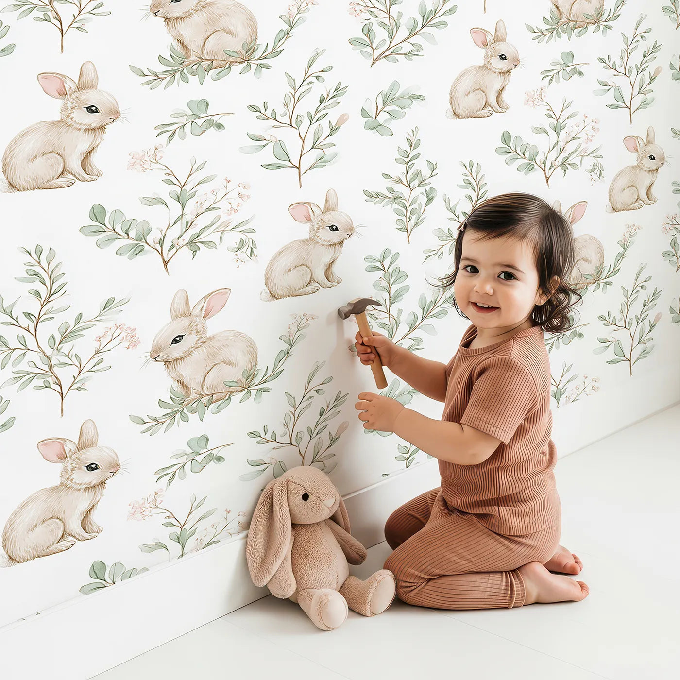 Lovely child standing in front of Whimsy Tots Bunny Garden Whispers Wallpaper with rabbit, leaf, flower, sprig in design.