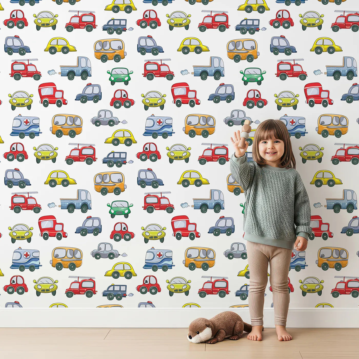 Lovely child standing in front of Whimsy Tots Tiny Wheels Parade Wallpaper in White with car, truck, bus, firetruck, ambulance in design.