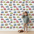 Lovely child standing in front of Whimsy Tots Tiny Wheels Parade Wallpaper in White with car, truck, bus, firetruck, ambulance in design. Lovely child standing in front of Whimsy Tots Tiny Wheels Parade Wallpaper in White with car, truck, bus, firetruck, ambulance in design.