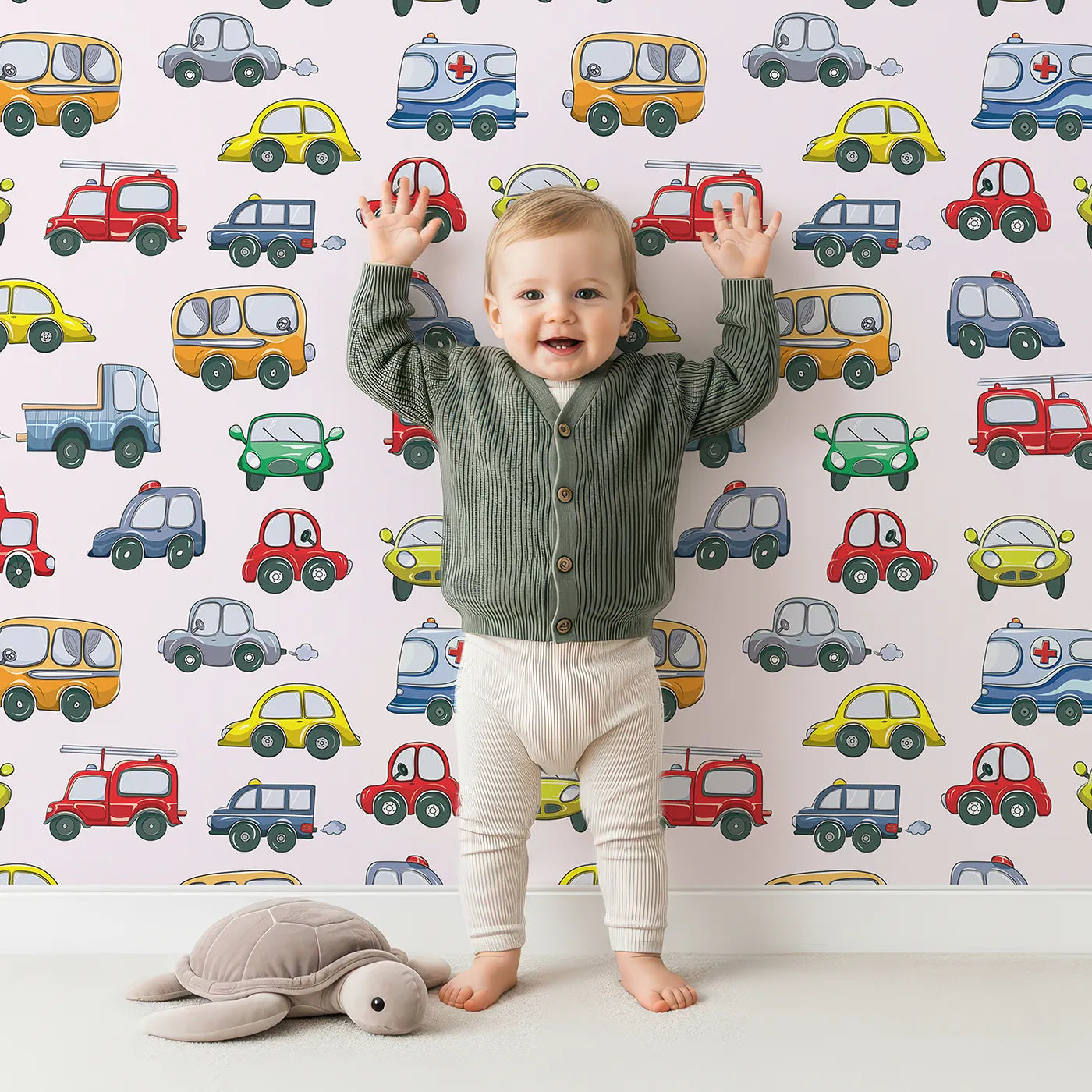 Lovely child standing in front of Whimsy Tots Tiny Wheels Parade Wallpaper in Soft Pink with car, truck, bus, firetruck, ambulance in design.