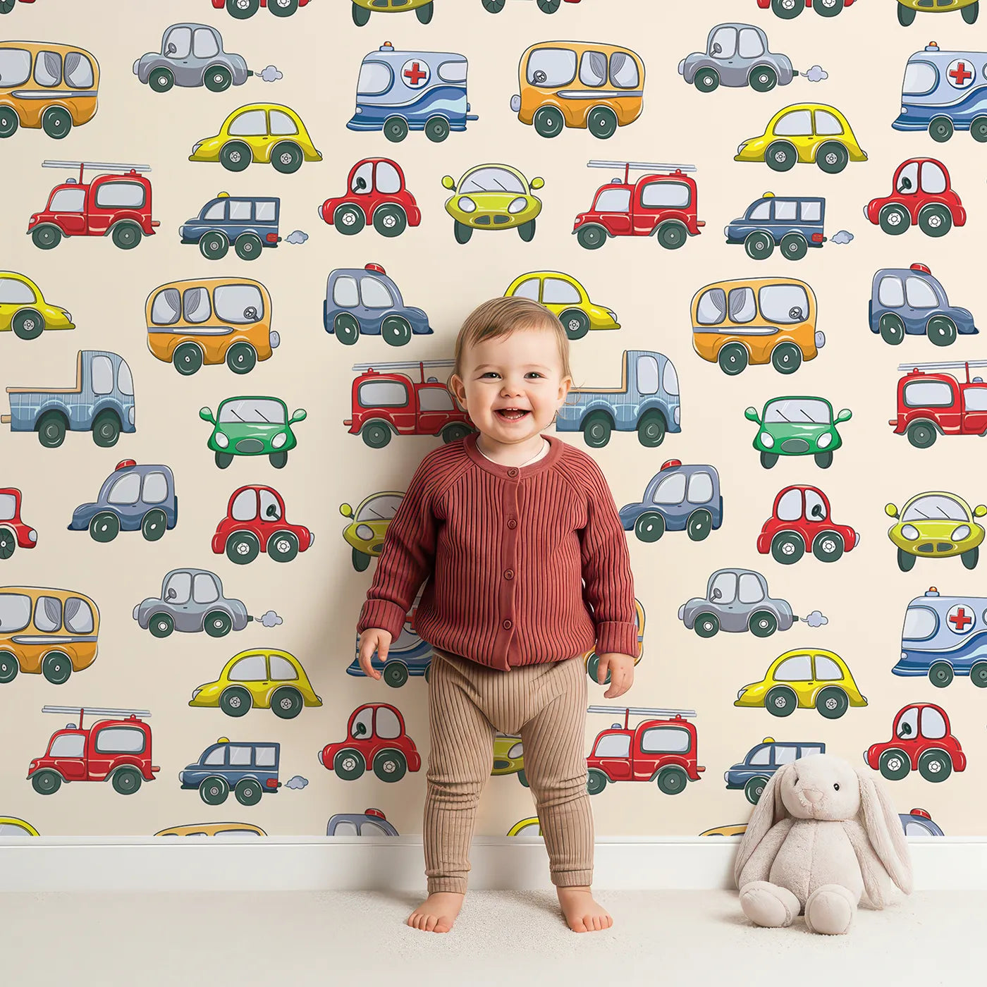 Lovely child standing in front of Whimsy Tots Tiny Wheels Parade Wallpaper in Cream with car, truck, bus, firetruck, ambulance in design.