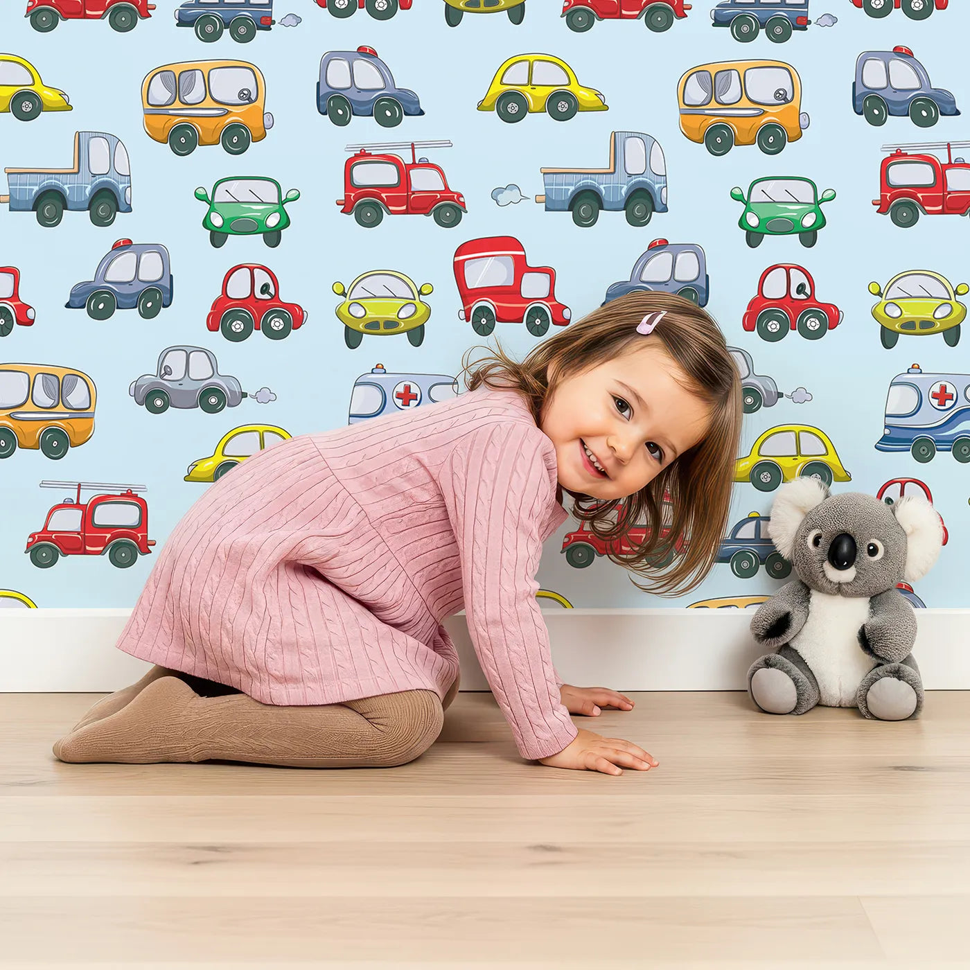 Lovely child standing in front of Whimsy Tots Tiny Wheels Parade Wallpaper in Sky Blue with car, truck, bus, firetruck, ambulance in design.