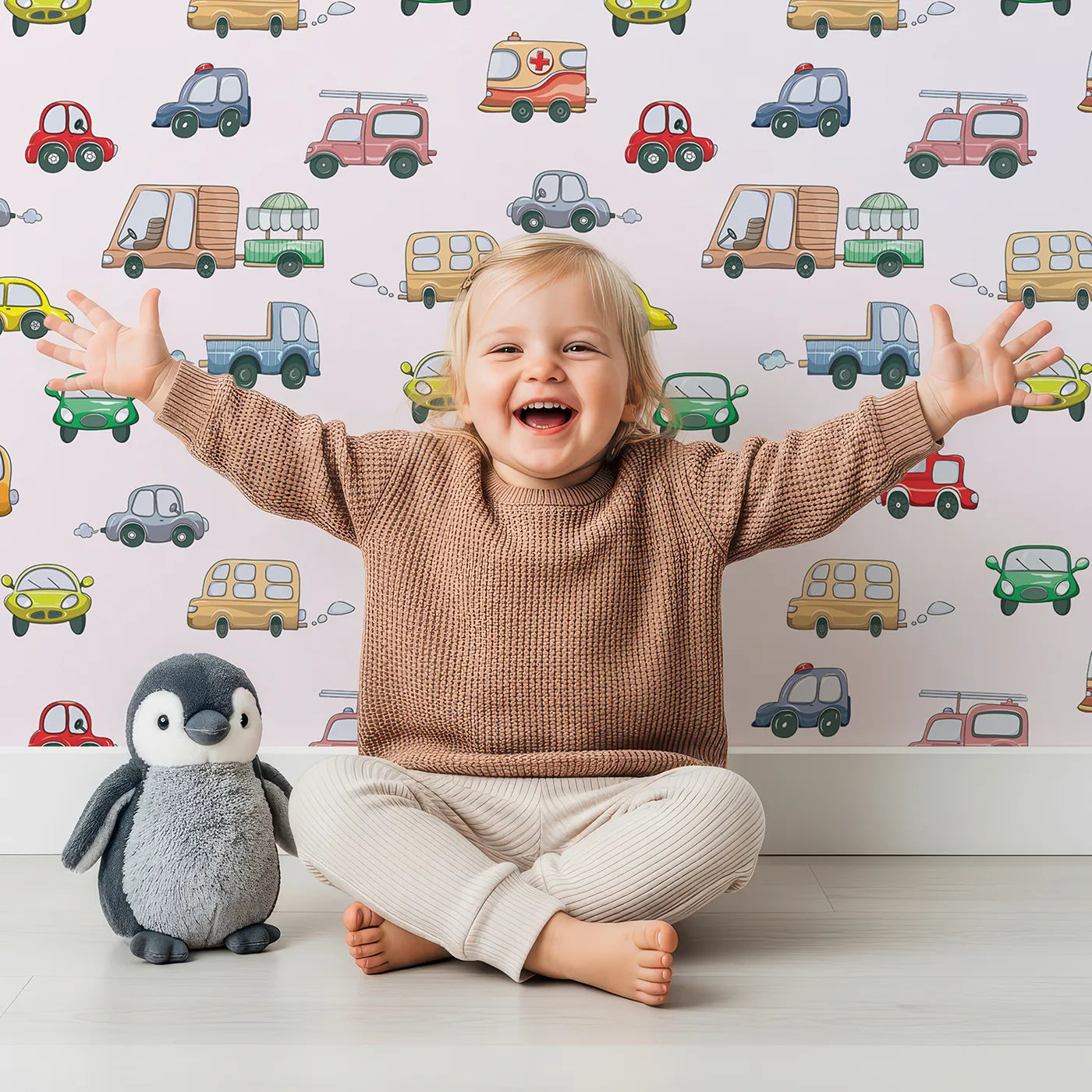 Lovely child standing in front of Whimsy Tots Bumper Buddies Rally Wallpaper in Soft Pink with car, truck, bus, foodtruck, taxi in design.