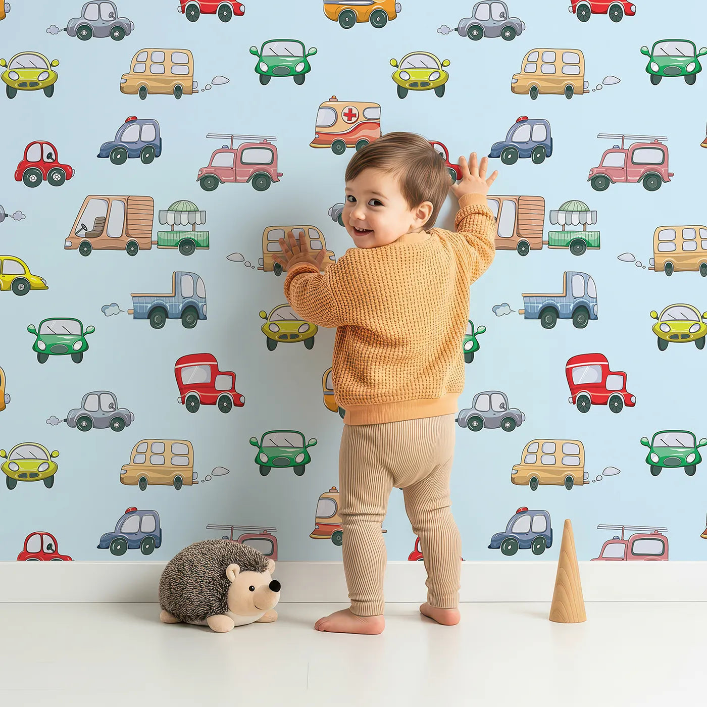 Lovely child standing in front of Whimsy Tots Bumper Buddies Rally Wallpaper in Sky Blue with car, truck, bus, foodtruck, taxi in design.
