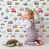 Lovely child standing in front of Whimsy Tots Bumper Buddies Forest Drive Wallpaper in White with car, tree, cloud, raindrop, bus in design. Lovely child standing in front of Whimsy Tots Bumper Buddies Forest Drive Wallpaper in White with car, tree, cloud, raindrop, bus in design.